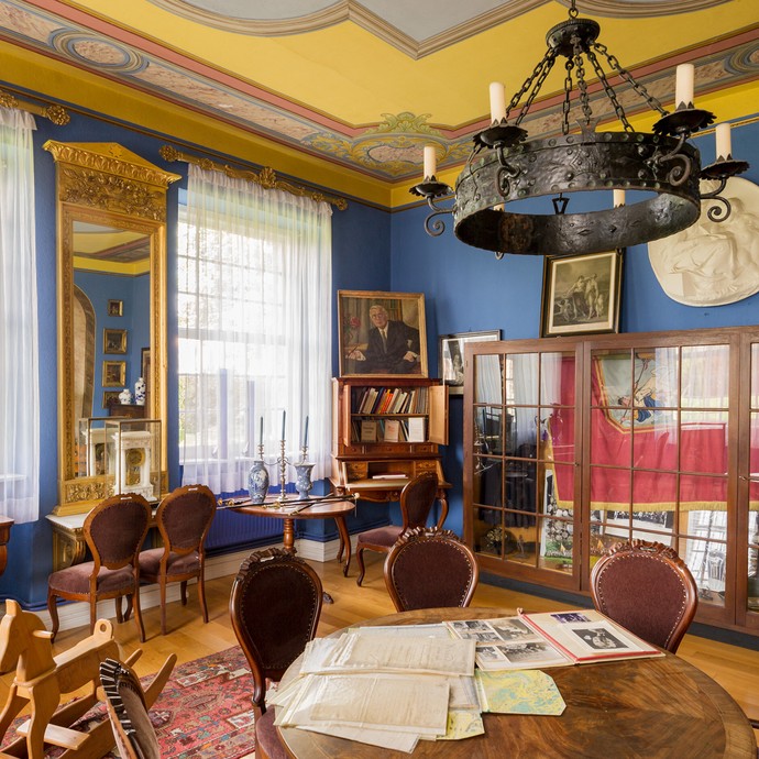 Im Haus gibt es einen Raum mit alten Holzmöbeln, großen Fenstern und blauen Wänden. Der Raum heißt Blauer Salon. (vergrößerte Bildansicht wird geöffnet)