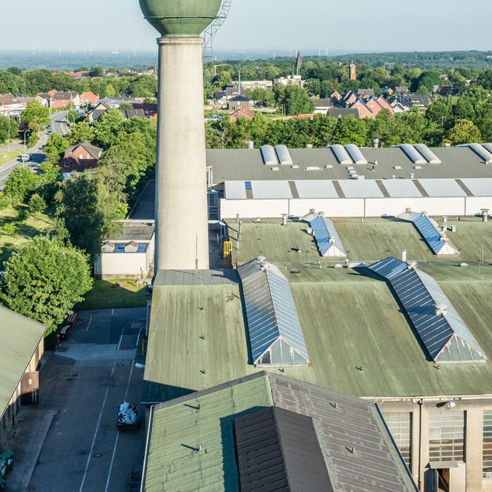 Blick von oben auf die stillgelegte Zeche. Die Dächer der Hallen sind hellgrün. Der hohe Wasserturm ragt hervor. (vergrößerte Bildansicht wird geöffnet)