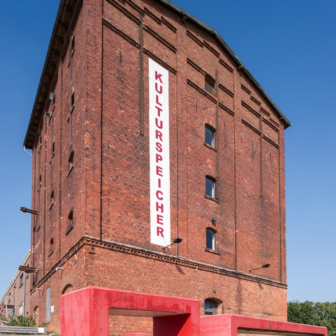 Blick auf das Gebäude. Auf einem weißen Schild steht von oben nach unten in roten Buchstaben "Kulturspeicher". (vergrößerte Bildansicht wird geöffnet)