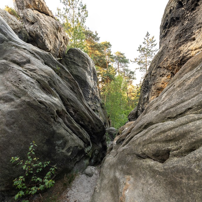 An beiden Seiten sind große graue Felsen. Dazwischen ist ein schmaler Spalt, durch den man grüne Bäume sieht. (vergrößerte Bildansicht wird geöffnet)