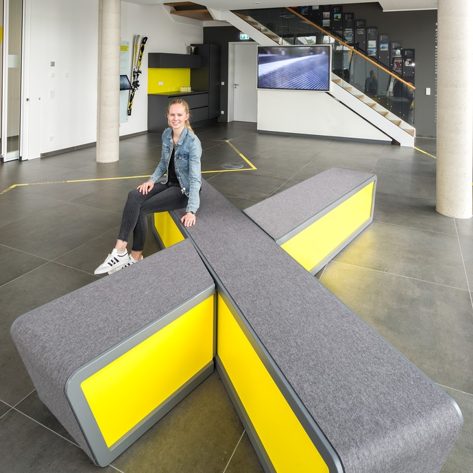 Katja Gehling arbeitet für die Saertex GmbH. Sie sitzt auf einer X-förmigen Bank im Foyer der Firma. (vergrößerte Bildansicht wird geöffnet)