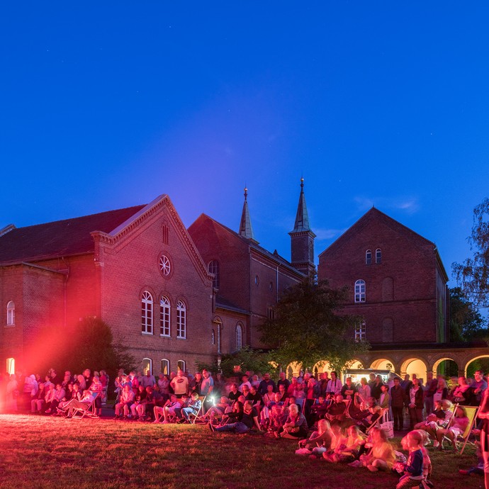 Vor dem Gebäude sind noch spätabends viele Menschen. Dieses Sommer-Event mit Live-Musik wird gut besucht. (vergrößerte Bildansicht wird geöffnet)