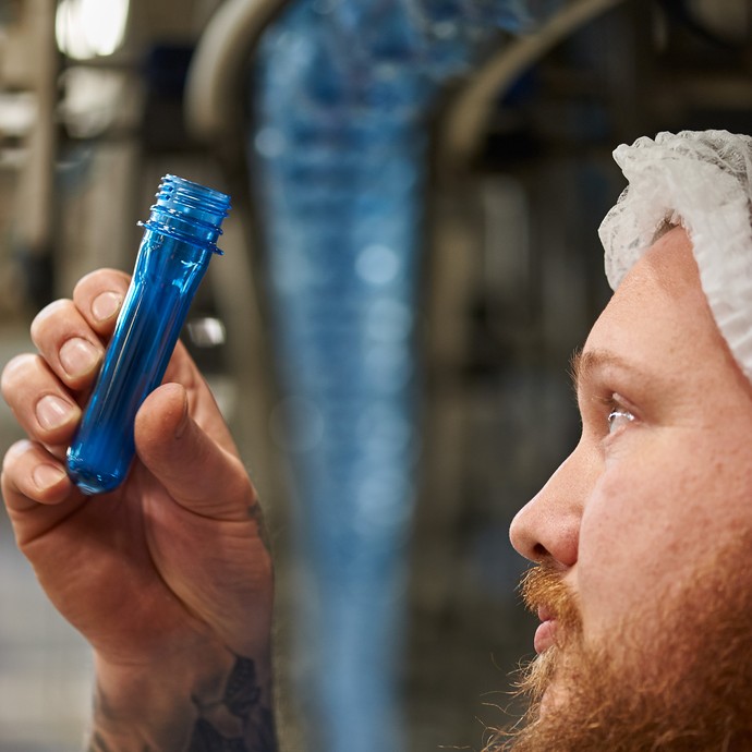Mitarbeiter Björn Koch hält eine blaue Plastikröhre. Er kontrolliert den Rohling, aus dem später eine Flasche wird. (vergrößerte Bildansicht wird geöffnet)