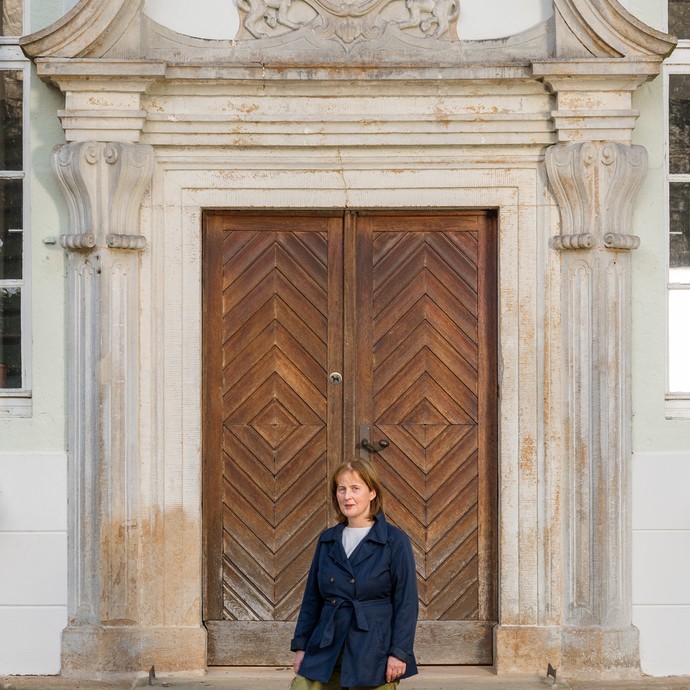 Die Referentin Dr. Christiane Kerrutt steht vor eine großen Eingangstür aus Holz. (vergrößerte Bildansicht wird geöffnet)