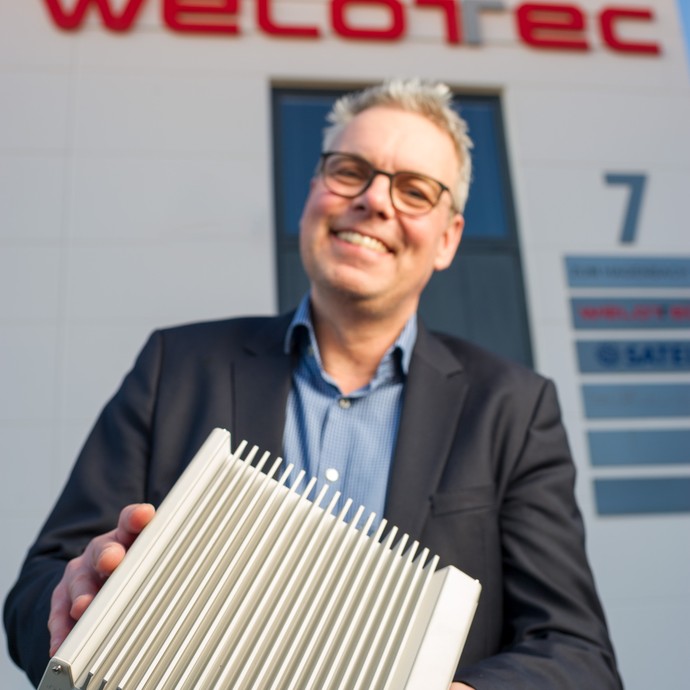 Der Geschäftsführer Reinhard Lülff zeigt freudig einen Industriecomputer. (vergrößerte Bildansicht wird geöffnet)