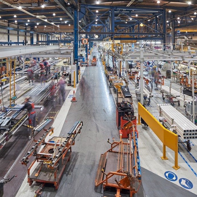 Große Halle, in der LKW-Teile produziert werden. Das Foto ist von oben mit Sicht auf die Arbeiter und LKW-Teile am Boden fotografiert. (vergrößerte Bildansicht wird geöffnet)