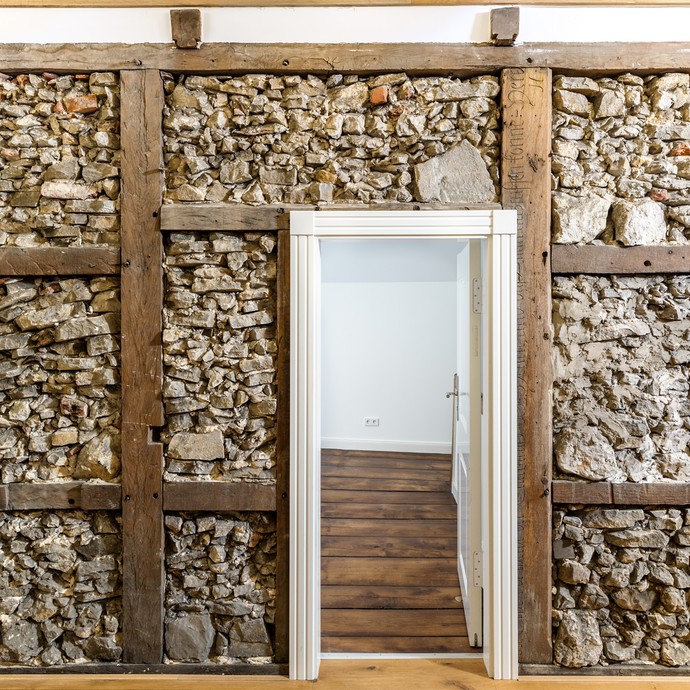 Eine helle Wand mit einer Tür in der Mitte. Holzbalken teilen die Wand in Fachwerk. Alte Burgsteine füllen die Fächer. (vergrößerte Bildansicht wird geöffnet)