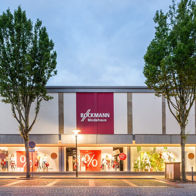 Außenfassade des Modhauses Böckmann in der Abenddämmerung. In den Schaufenstern sind Schilder mit Rabattangeboten. (vergrößerte Bildansicht wird geöffnet)