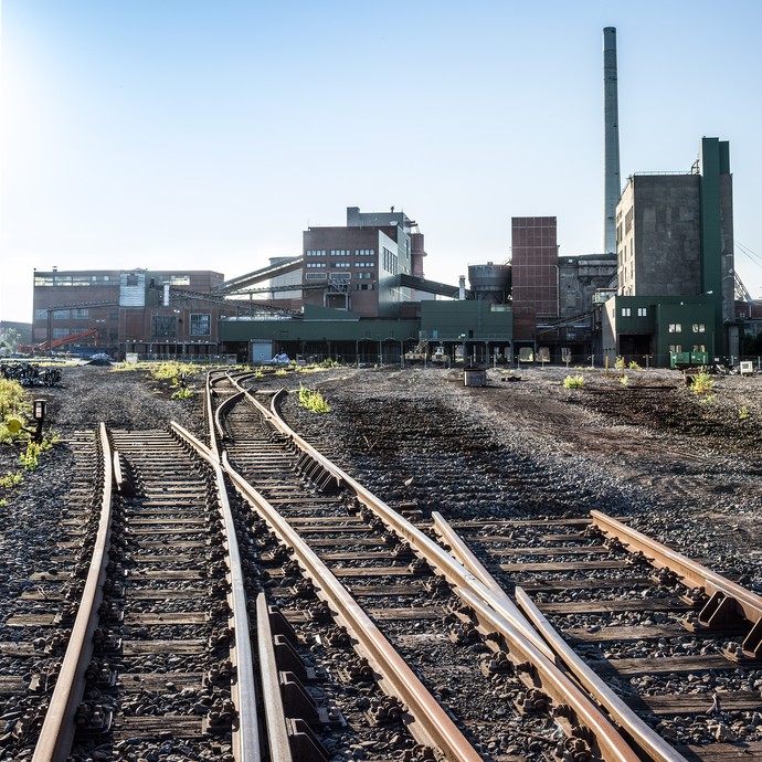 Im Vordergrund drei Bahnschienen, die auf den unteren Bildrand zulaufen. Im Hintergrund ist das stillgelegte Zechengebäude. (vergrößerte Bildansicht wird geöffnet)