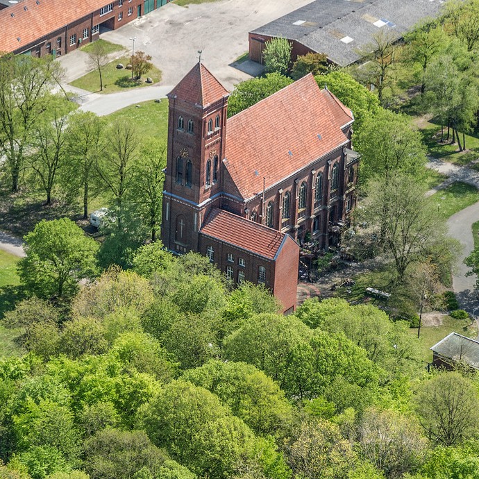 Luftaufnahme der Kunstkirche am St. Josefshaus. Um die rötliche Kirche herum sind alte Bäume und Hofanlagen zu sehen. (vergrößerte Bildansicht wird geöffnet)