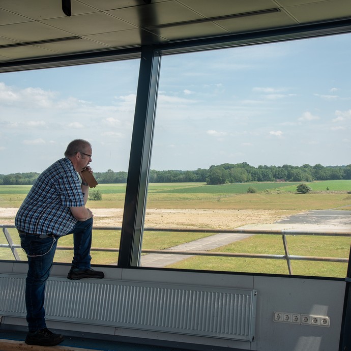 Im alten Flugverkehrskontrollturm steht Herr Jung vor einem Fenster und telefoniert. Er schaut nach draußen auf die Startbahn. (vergrößerte Bildansicht wird geöffnet)