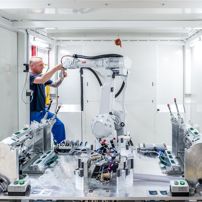 Andre Buchholz arbeitet an einem weißen Roboterarm. Das ist ein Schneideroboter für Türverkleidungen. (vergrößerte Bildansicht wird geöffnet)