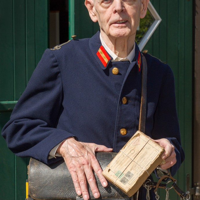 Porträtaufnahme des ehemaligen Postbeamten Klemens Beckemeyer. Er trägt seine ehemalige Arbeitskleidung mit brauner Ledertasche. (vergrößerte Bildansicht wird geöffnet)