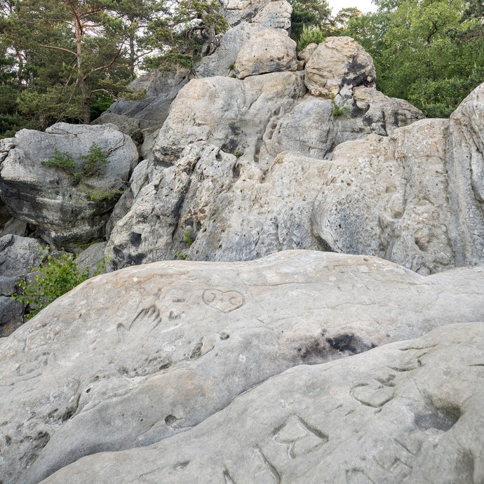 Im Vordergrund graue Felsen, in die Buchstaben eingeritzt sind. Im Hintergrund aufgetürmte kleine Felsen. Dahinter viele grüne Bäume. (vergrößerte Bildansicht wird geöffnet)