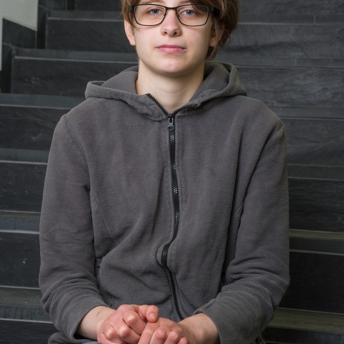 Porträtbild von der Schülerin Michelle (17). Sie sitzt auf einer Treppe und trägt einen grauen Pullover. (vergrößerte Bildansicht wird geöffnet)