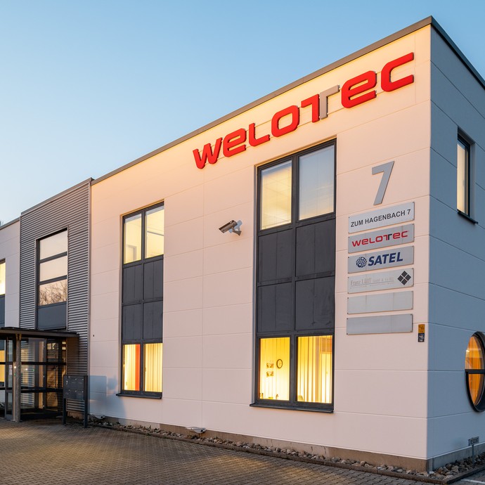 Das rechteckige Firmengebäude in der Abendsonne. Rechts oben steht in roter Schrift „Welotec“. (vergrößerte Bildansicht wird geöffnet)