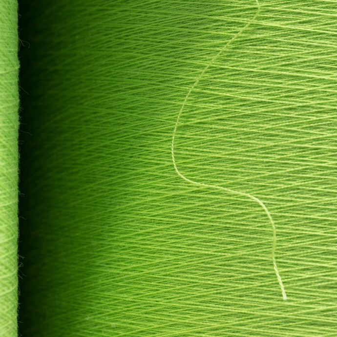 Nahaufnahme einer Stoffgarnrolle. Die einzelnen grünen Fäden sind deutlich zu erkennen. (vergrößerte Bildansicht wird geöffnet)