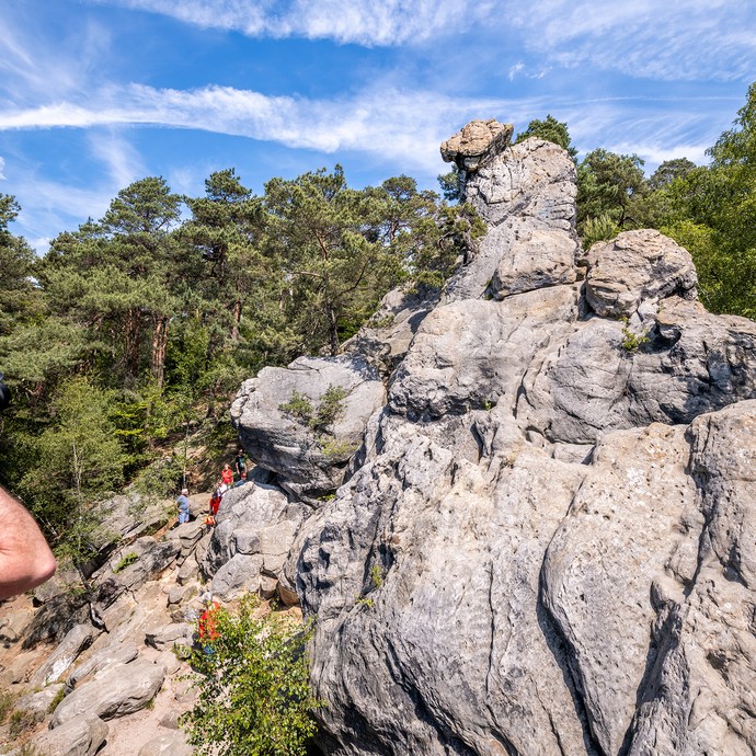 Einzelne Menschen in bunter Kleidung auf einem großen grauen Felsen. Im Vordergrund fotografiert ein Mann die Szene. (vergrößerte Bildansicht wird geöffnet)