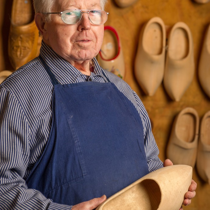 Engelbert Thünte zeigt den fertigen Holzschuh. Die traditionelle Arbeitsbekleidung ist ein gestreiftes Hemd mit blauer Schürze. (vergrößerte Bildansicht wird geöffnet)