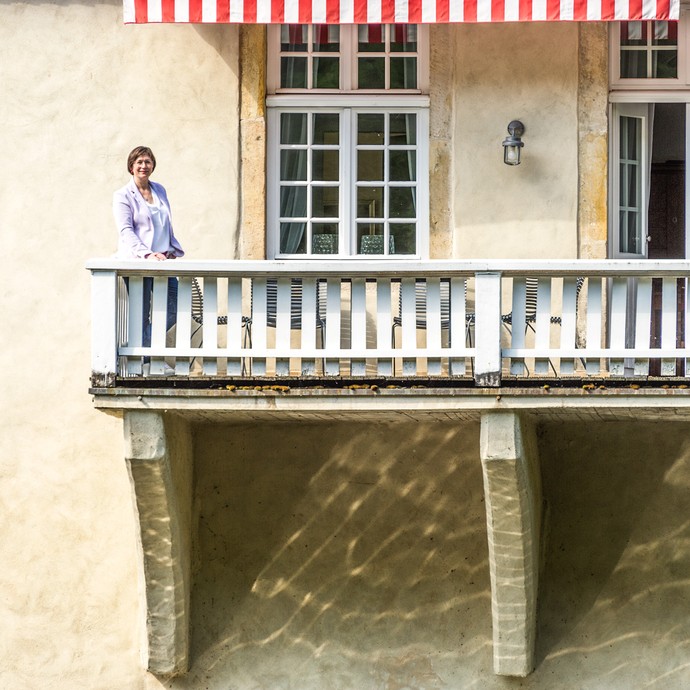 Auf dem Balkon des hellen Schlosses steht eine Frau in der Sonne. Frau Ricarda Freifrau von Diepenbroick-Grüter ist die Hausherrin. (vergrößerte Bildansicht wird geöffnet)