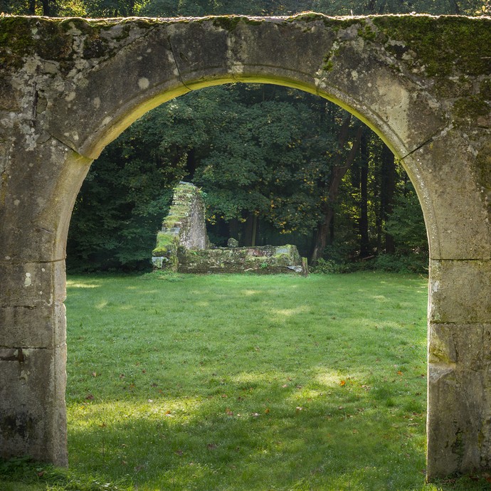 Blick durch einen alten Torbogen aus Stein. Moos wächst darauf. Im Hintergrund stehen die Ruinen der ehemaligen Vorburg. (vergrößerte Bildansicht wird geöffnet)