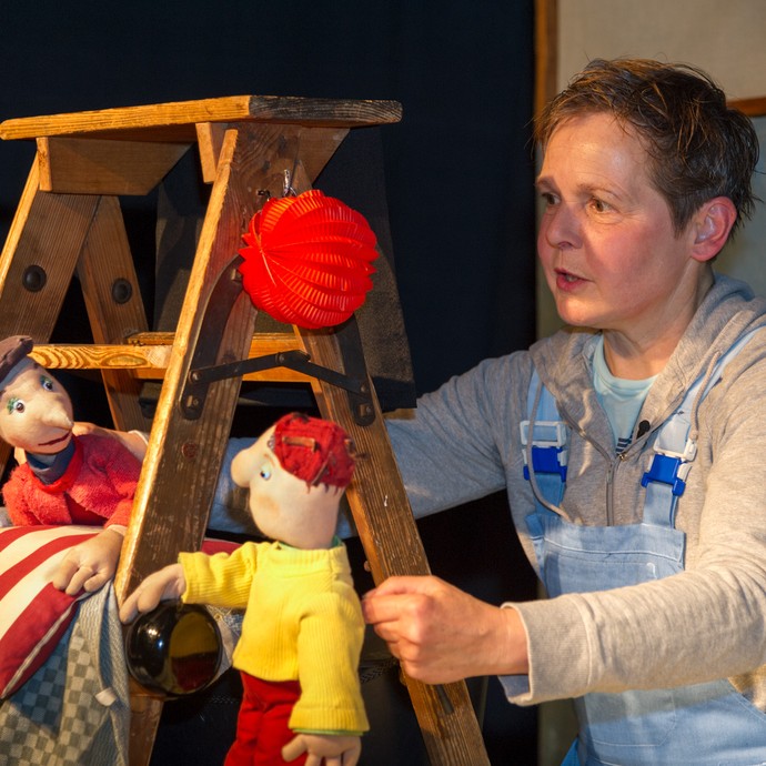 Eine Frau hält zwei Theaterpuppen in den Händen. Sie führt ein Stück auf. Die Puppen tragen bunte Kleidung. (vergrößerte Bildansicht wird geöffnet)