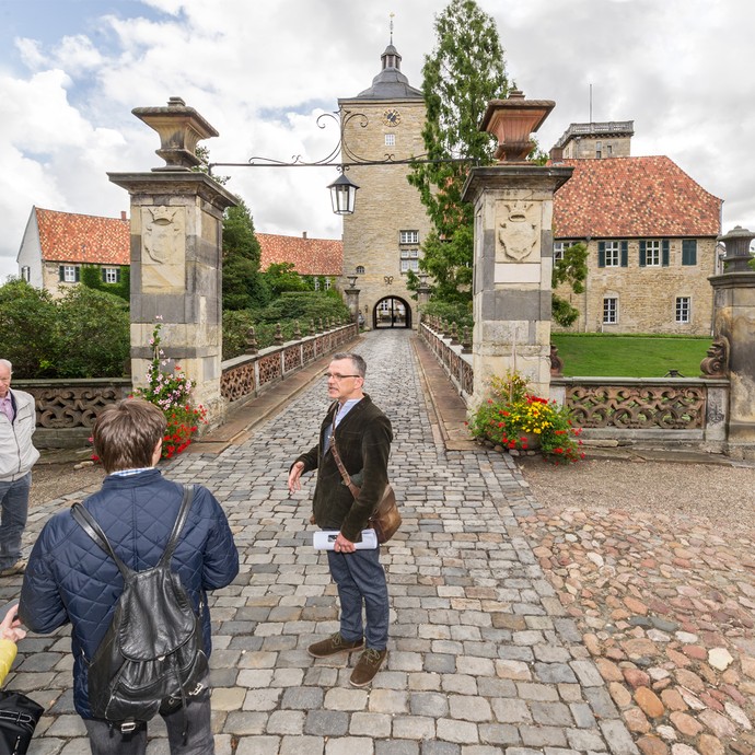 Fünf Personen stehen vor einem Torbogen. Hinter dem Torbogen führt ein langer Weg zum Schloss Burgsteinfurt. (vergrößerte Bildansicht wird geöffnet)