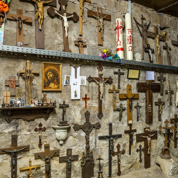 Im Kreuzkeller unter der Basilika hängen viele Kreuze an der Wand. Sie sind alle verschieden. An einigen hängt eine Jesus-Figur. (vergrößerte Bildansicht wird geöffnet)