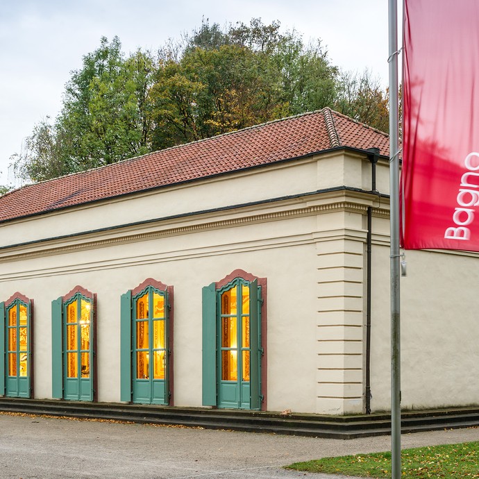 Außenansicht eines hellen Gebäudes mit vielen Fenstern. Rechts weht eine rote Fahne. Darauf steht "Bagno Konzertgalerie". (vergrößerte Bildansicht wird geöffnet)