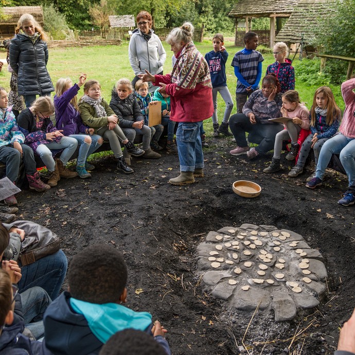 Eine Schulklasse sitzt im Kreis um einige Steine. Auf den erhitzten Steinen wird Fladenbrot gebacken. (vergrößerte Bildansicht wird geöffnet)