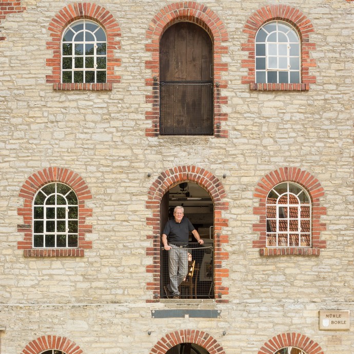 Außenfassade mit Fenstern und drei Türen. In der mittleren Tür steht Werner Schwentker, der Vorsitzende des Mühlenvereins. (vergrößerte Bildansicht wird geöffnet)